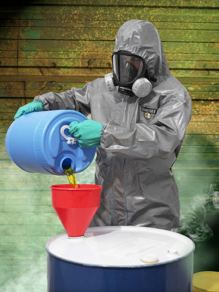 Un trabajador que lleva ropa de protección química ChemMax está vertiendo un producto químico en forma de vapor en un barril.