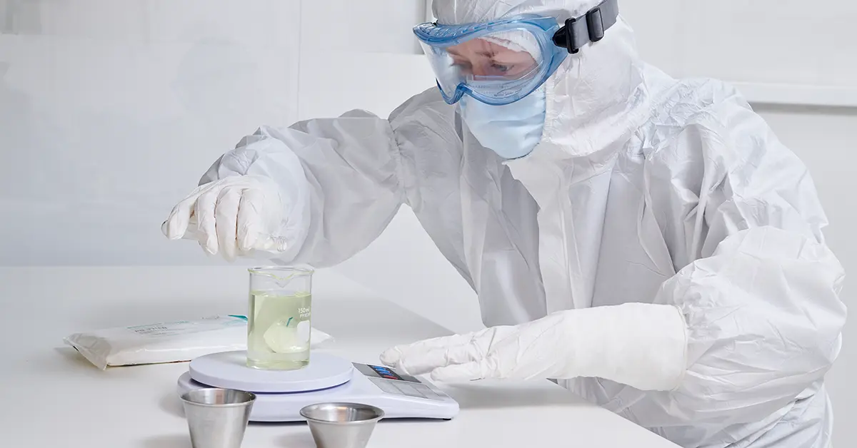 working in a cleanroom, a lab technician is looking at a beaker filled with liquid. They are wearing cleanroom ppe, CleanMax by Lakeland Industries