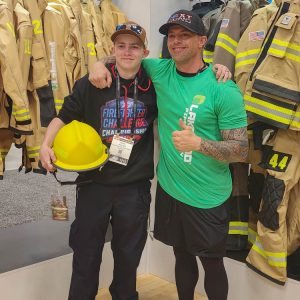 Two smiling men at firefighter gear exhibit.