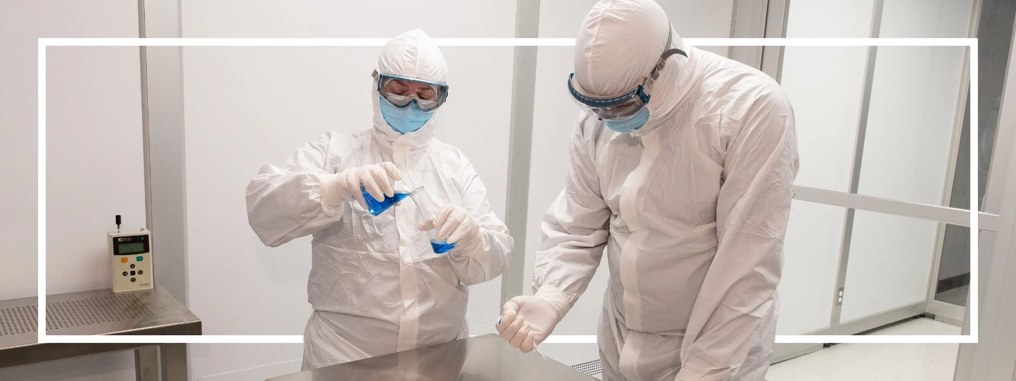 Two cleanroom workers don Lakeland's CleanMax disposable garments while pouring liquid chemicals between beakers and pipettes