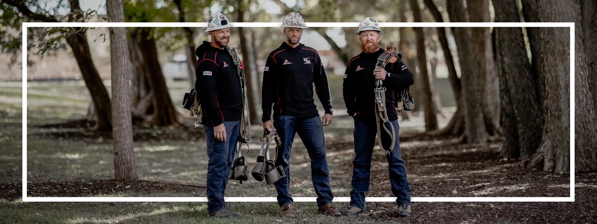 Three smiling utility workers standing among trees wearing the black waffle knit from Lakeland's HPFR line