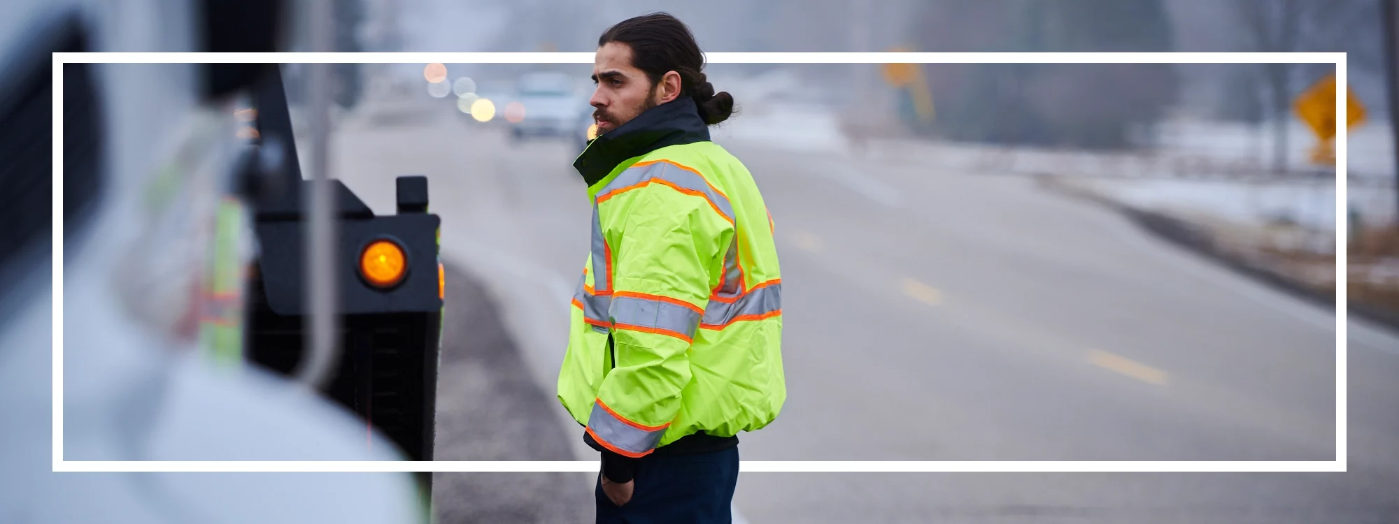 Bild eines Abschleppwagenfahrers, der auf dem Mittelstreifen einer stark befahrenen Autobahn steht und eine Jacke aus der Reihe der Warnschutzkleidung von Lakeland trägt