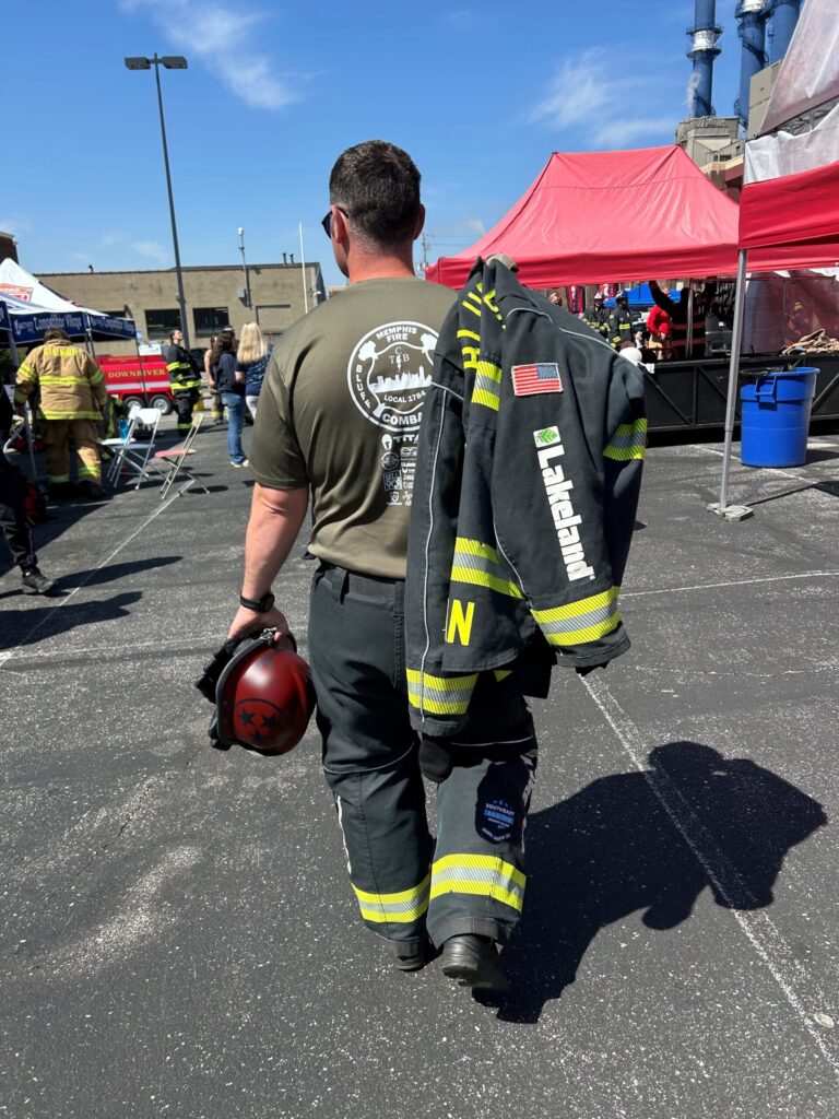 Firefighter carrying helmet, jacket at outdoor event.