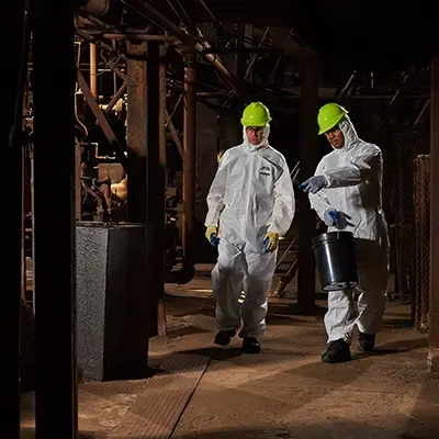 Industrial Workers wearing Lakeland SafeGard GP for protection, walking past industrial equipment and iron beams.